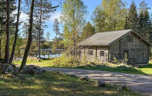 A rustic log cabin with a dirt path leading to it, surrounded by trees and a body of water in the background. - 4 bedroom pet friendly home in Fegen (Fegen)