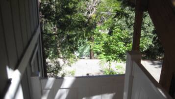 A view from a covered porch with a wooden railing, looking out to a garden area with trees and a pathway.