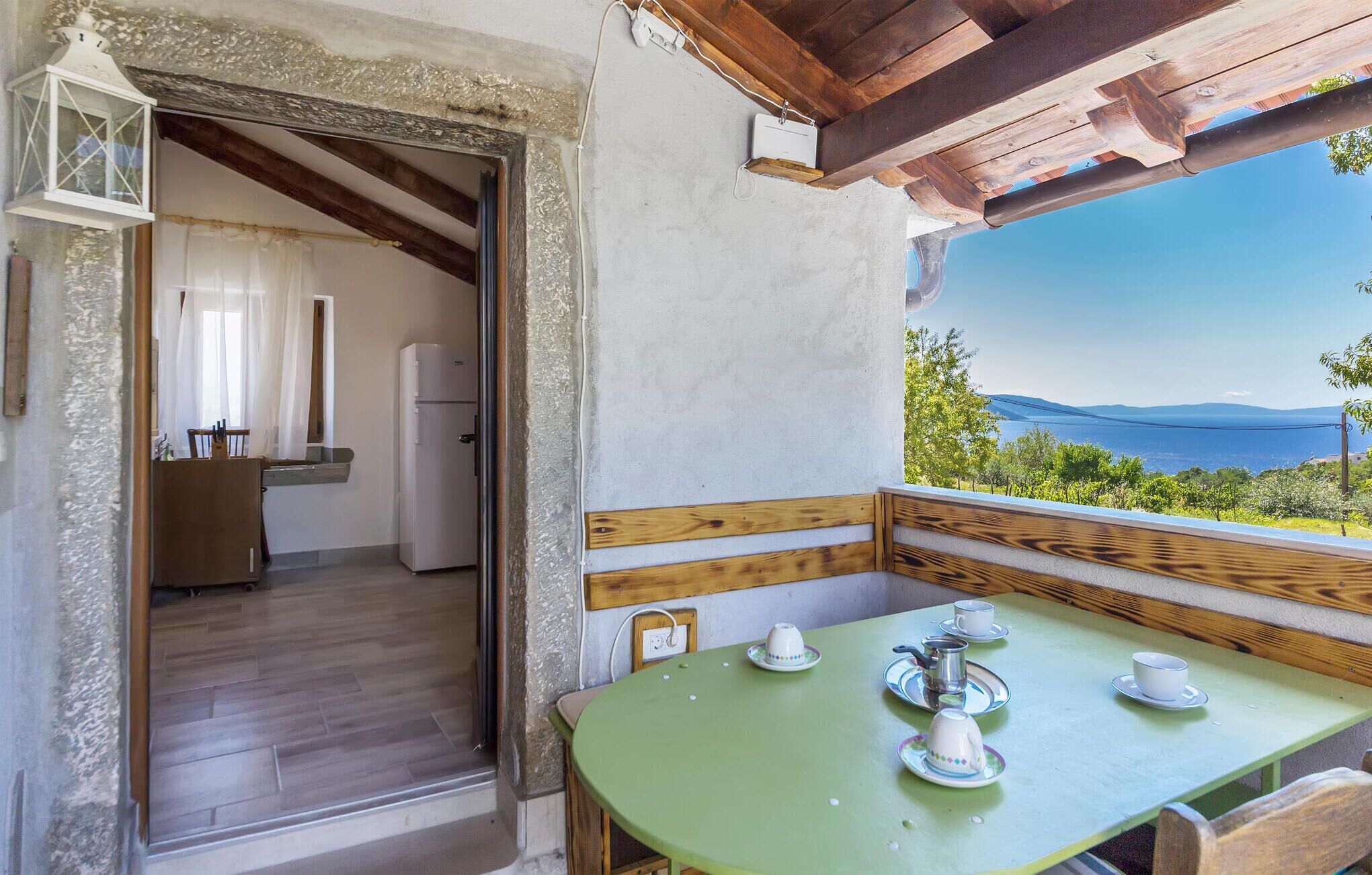 Una habitación acogedora con un banco de madera y una mesa lista para el té, una zona de cocina con refrigerador y una vista panorámica del mar.