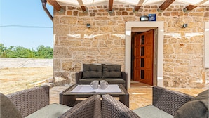Habitació amb parets de pedra, una porta de fusta, mobles de vímet i una taula amb tasses.
