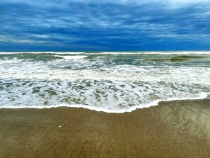 A beach with waves crashing onto the shore under a cloudy sky.