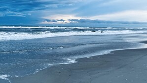 Een strand met golven die de kust naderen onder een bewolkte lucht.