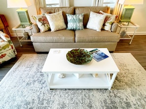 A living room with a beige sofa, patterned cushions, a white coffee table, and a decorative bowl.