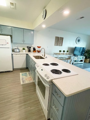 A modern kitchen with white appliances, a dining area with a table and chairs, and a TV in the background.