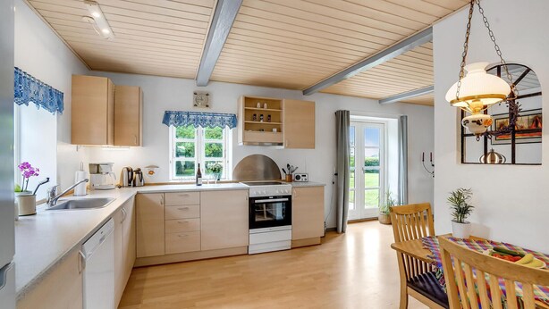Una cucina moderna con mobili impiallacciati in legno, forno integrato e zona pranzo con tavolo e sedie in legno.