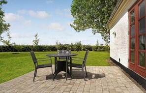 Une terrasse avec une table ronde et des chaises, une bouteille de vin et un verre.
