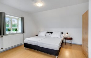 Une chambre à coucher avec un lit double, une table de chevet avec une lampe, un radiateur et une fenêtre avec des rideaux.