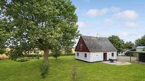 Una piccola casa bianca con tetto rosso, circondata da erba verde e alberi.