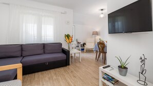 Un salon moderne avec un canapé gris, une table basse blanche, un téléviseur fixé au mur et une petite bibliothèque.