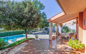 A covered patio with a pool, outdoor seating, and a large tree.