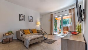 Un salon moderne avec un canapé, une petite table d’appoint ornée d’une plante, une lampe et une vue sur la terrasse extérieure.