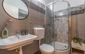 A bathroom with a shower, toilet, sink, and a mirror.