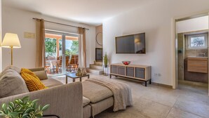 Un salon comprenant un canapé, un téléviseur fixé au mur, un coin repas avec des chaises et une table, ainsi qu’une cuisine équipée d’un évier et de placards.