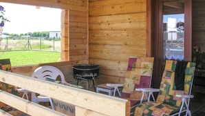 Eine Holzhütte mit Veranda, Grill und zwei bunten Stühlen.