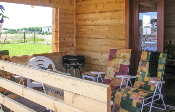 Una cabaña de madera con un porche, una parrilla y dos sillas de colores.
