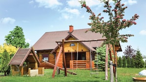 Eine Holzhütte mit geneigtem Dach, einer Veranda und einem kleinen Holzgebilde zur Linken.