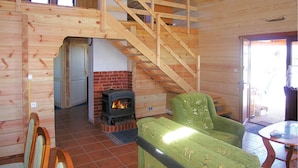 Ein Holzblockhaus-Innenraum mit Kamin, einem grünen Sessel, einer Holztreppe und einer Tür zu einem anderen Raum.