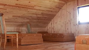 Eine Holzhütte mit geneigtem Dach, einem Fenster und einer schlichten Einrichtung mit einem Sessel und zwei Sofas.