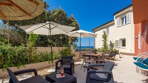 An outdoor patio with wicker furniture, umbrellas, and a view of the sea.