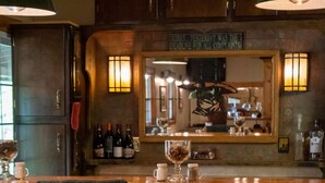 Una zona de bar con taburetes de madera y una barra, con un letrero sobre el espejo y botellas de alcohol en la barra.