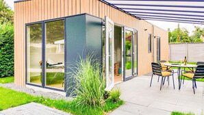 Ett modernt hus med stora skjutbara glasdörrar, en uteplats med bord och stolar samt en trädgårdsdel med gräsmatta och växter.