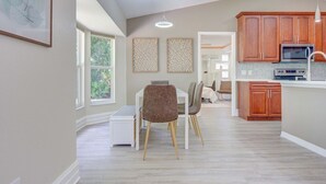A modern kitchen with wooden cabinets, a built-in microwave, and a dining area with a white table and two chairs.
