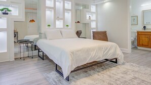 A bedroom with a bed, a desk, and a chair. There is a ceiling fan and a window with a view of the outside.