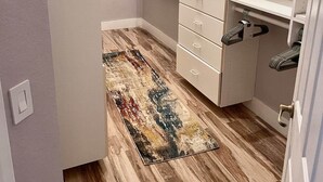 Un vestidor con estanterías blancas, un suelo de madera y una alfombra estampada.