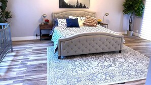 Un dormitorio con cabecera capitonada, colcha estampada y un ventanal con persianas.