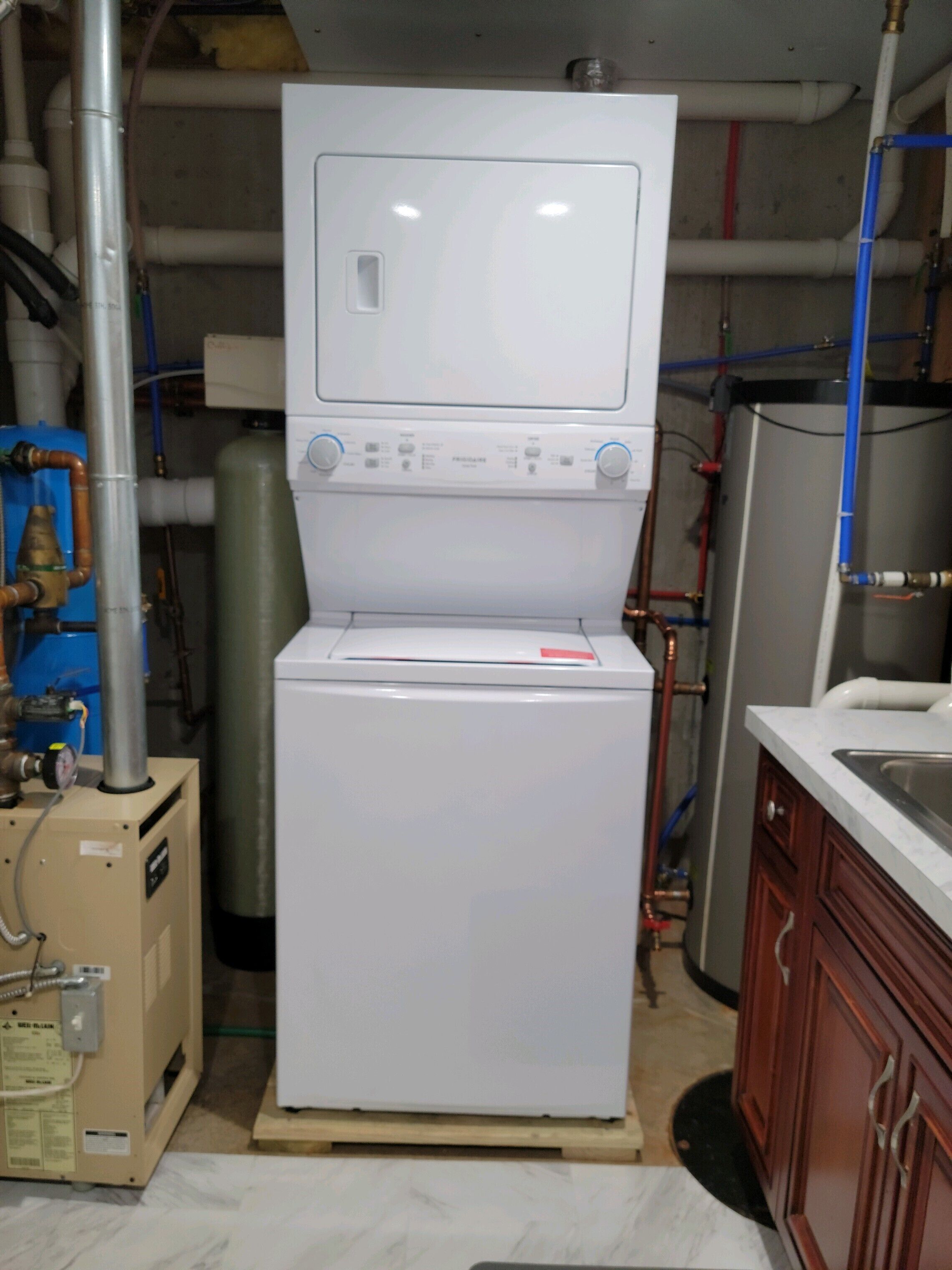 A compact, white laundry machine in a utility room with visible pipes and a water heater.