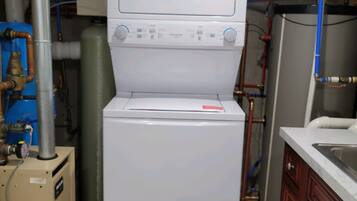 A compact, white laundry machine in a utility room with visible pipes and a water heater.