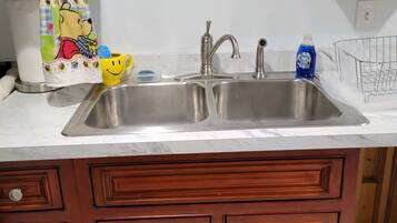 A kitchen with a double stainless steel sink, wooden cabinets, a towel with a cartoon character, a yellow mug, and a dish soap bottle.