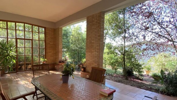 A covered patio with a round table and chairs, surrounded by potted plants and a brick wall. - Apartment Sonia by Interhome (Riparbella)