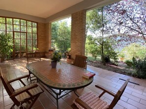 A covered patio with a round table and chairs, surrounded by potted plants and a brick wall. - Apartment Sonia by Interhome (Riparbella)