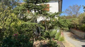 A modern building with a white exterior and red-tiled roof, surrounded by lush greenery and a gravel pathway. - Apartment Sonia by Interhome (Riparbella)
