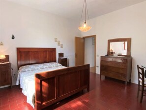 A bedroom with a wooden bed, a dresser, a mirror, and a hanging light fixture. - Apartment Sonia by Interhome (Riparbella)