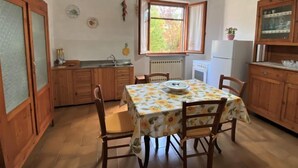 A compact kitchen with wooden cabinets, a dining table with floral tablecloth, and a window providing natural light. - Apartment Sonia by Interhome (Riparbella)