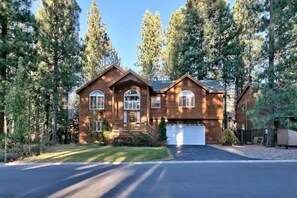 A two-story wooden house with a garage, surrounded by tall pine trees.
