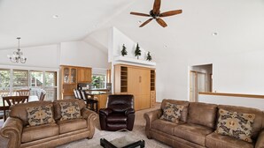 Ein geräumiges Wohnzimmer mit zwei braunen Ledersofas, einem Glastisch und einem Deckenventilator.