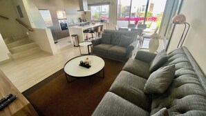 Un salon moderne avec un canapé gris, une table basse et une cuisine en arrière-plan.