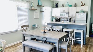 A kitchen with white cabinets, a wooden dining table with benches, and a small island with a sink. - Sunset Beach, on the golf course, pet friendly. (Sunset Beach)