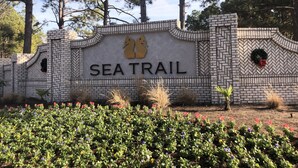 A brick wall with the words "SEATRAIL" and a logo, surrounded by greenery and flowers. - Sunset Beach, on the golf course, pet friendly. (Sunset Beach)