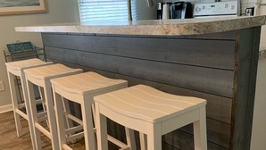 A kitchen with a wooden bar stool seating area, white cabinets, and a microwave. - Sunset Beach, on the golf course, pet friendly. (Sunset Beach)