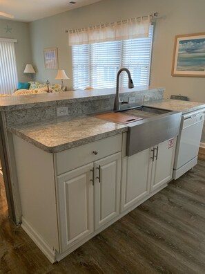 A kitchen with a granite countertop, white cabinetry, a stainless steel sink, and a window with blinds.