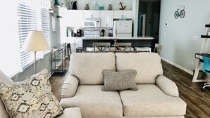 A modern living room with a sofa, a coffee table, and a lamp. There is a kitchen in the background with a refrigerator, microwave, and cabinets. - Sunset Beach, on the golf course, pet friendly. (Sunset Beach)