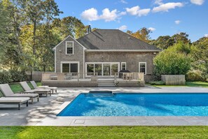 Une maison à deux étages avec une piscine, des chaises longues et un jardin clôturé.