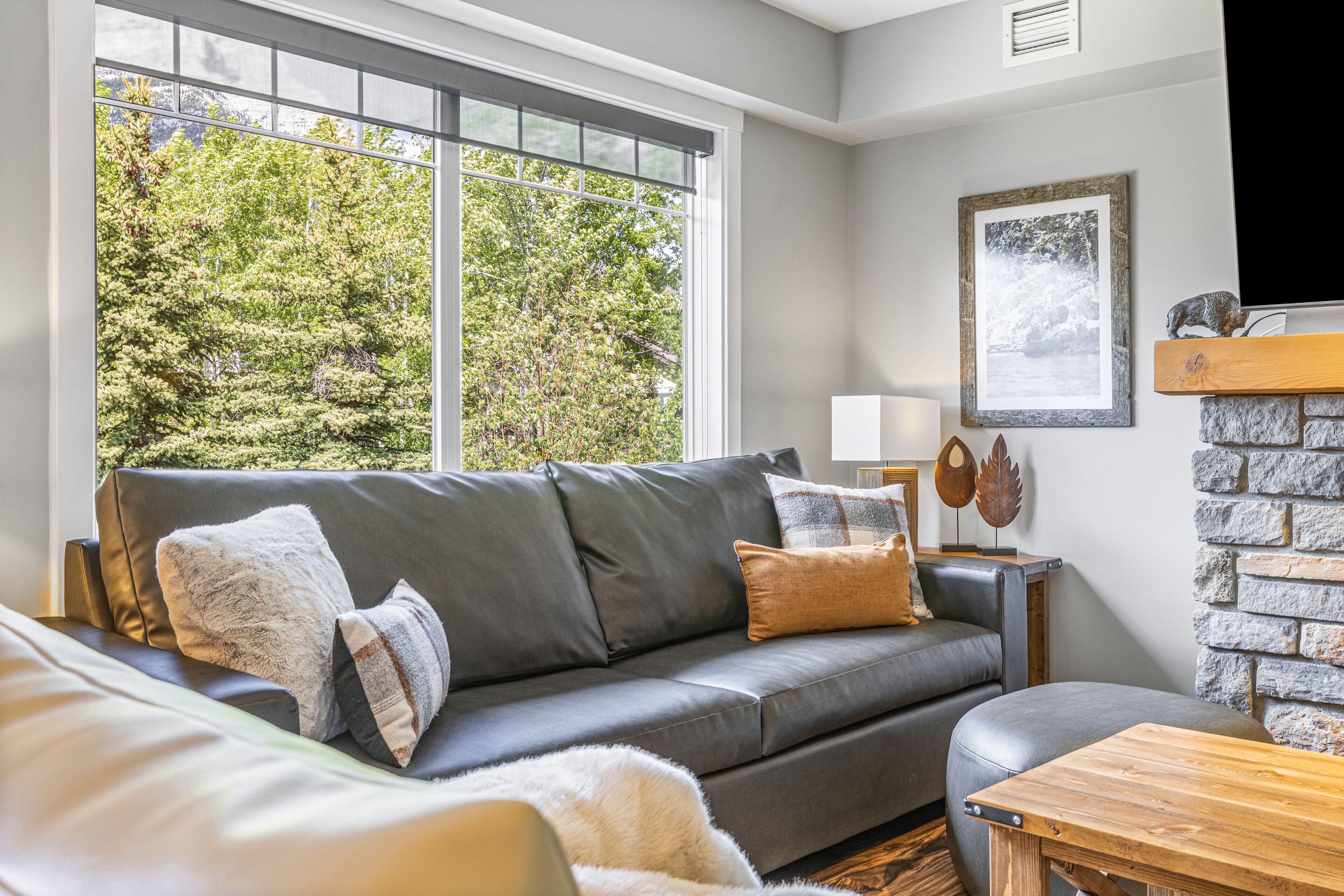 A modern living room with a grey leather sofa, a wooden coffee table, and a stone fireplace.