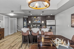 A modern kitchen with dark cabinets, a stainless steel refrigerator, and a central island with bar stools. - Rocky Mountain Condo, Grotto Mtn Views, Hot Tub (Dead Man's Flats)