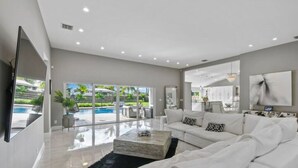 A spacious living room with a white sofa, a coffee table, and a TV mounted on the wall. - Luxury Unique Property 4-3 - Entire House - Heated Pool - Lg Yard (West Palm Beach)