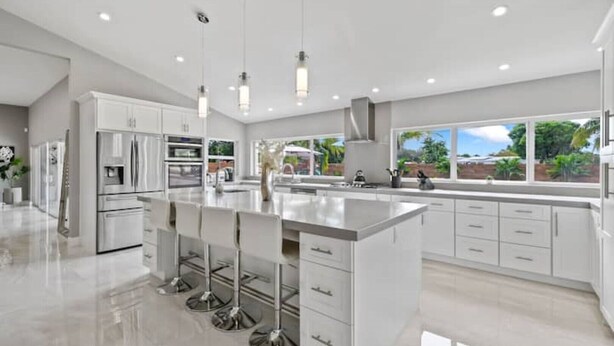 A modern kitchen with a central island, stainless steel appliances, and a large window providing a view of the outdoors. - Luxury Unique Property 4-3 - Entire House - Heated Pool - Lg Yard (West Palm Beach)